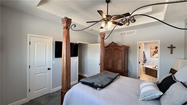 bedroom featuring a raised ceiling, visible vents, carpet flooring, ensuite bath, and baseboards