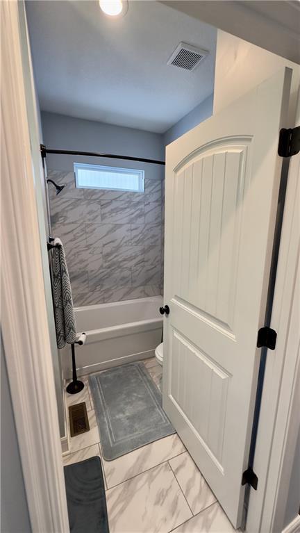 full bathroom featuring toilet, marble finish floor, washtub / shower combination, and visible vents