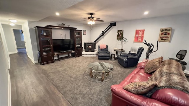 living area with recessed lighting, dark wood-type flooring, a ceiling fan, baseboards, and a wood stove