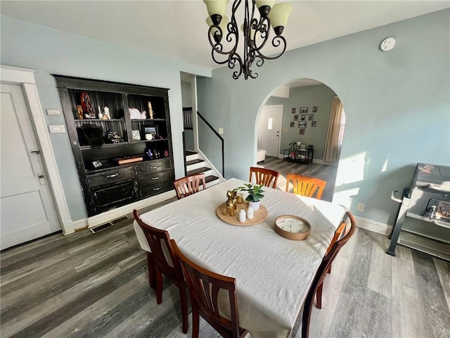 dining area featuring arched walkways, stairway, dark wood finished floors, and a notable chandelier