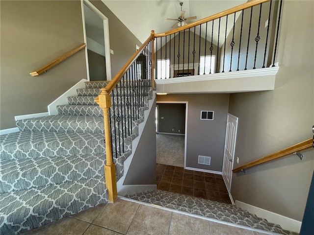 stairs with high vaulted ceiling, visible vents, baseboards, and a ceiling fan