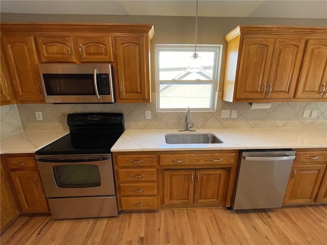 kitchen with appliances with stainless steel finishes, light wood-type flooring, brown cabinets, and a sink