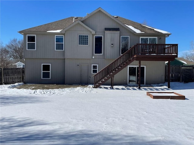 snow covered rear of property with a shingled roof, stairway, and fence