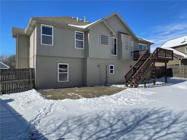 snow covered rear of property with stairs, fence, and a deck