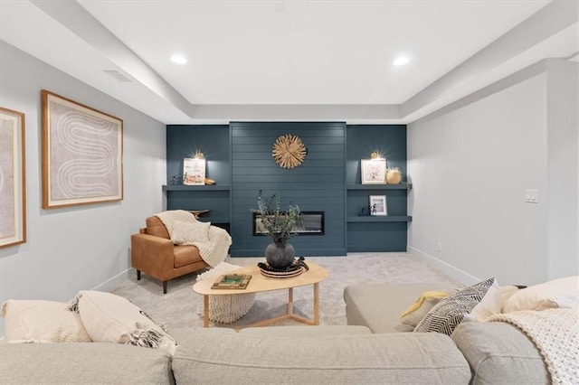 carpeted living room with baseboards, visible vents, a fireplace, and a tray ceiling