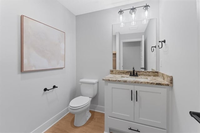 half bathroom featuring toilet, vanity, wood finished floors, and baseboards
