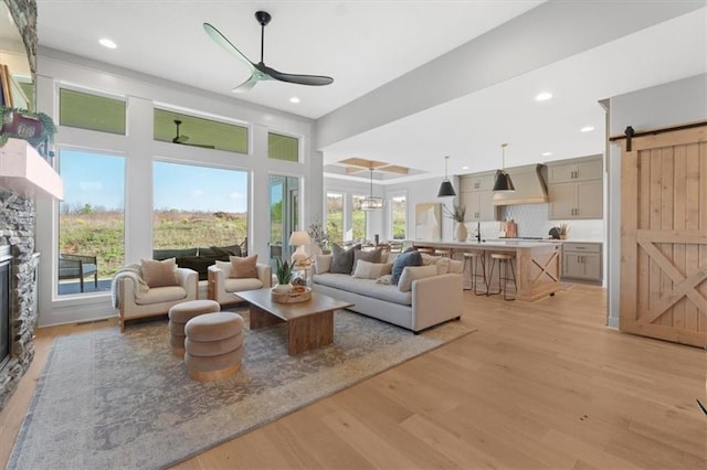 living room featuring a barn door, ceiling fan, light wood-type flooring, recessed lighting, and a fireplace