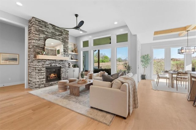living room featuring light wood-style floors, baseboards, recessed lighting, a stone fireplace, and ceiling fan with notable chandelier