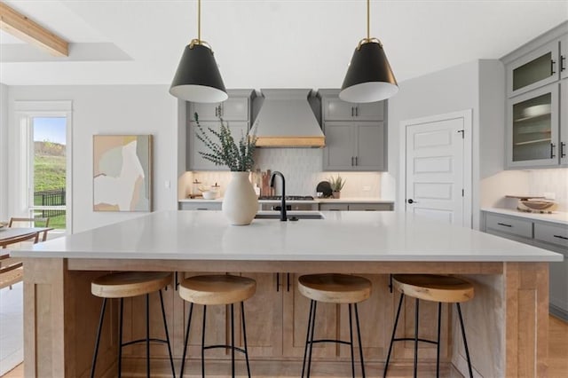 kitchen featuring gray cabinetry, light countertops, backsplash, and wall chimney range hood