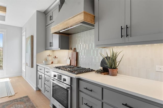 kitchen featuring gray cabinets, light wood-type flooring, light countertops, premium range hood, and appliances with stainless steel finishes