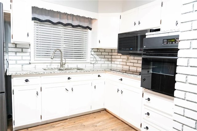 kitchen with light stone countertops, white cabinets, a sink, and black oven