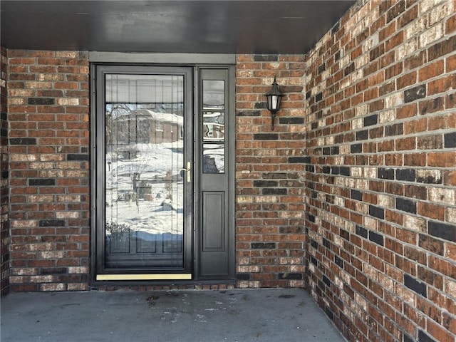 snow covered property entrance featuring brick siding