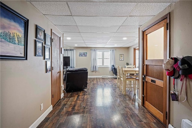 hallway featuring dark wood-style flooring, a drop ceiling, visible vents, and baseboards