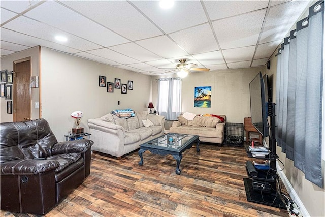 living area with a ceiling fan, a drop ceiling, and dark wood finished floors