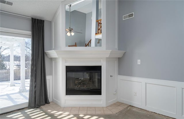 details featuring a glass covered fireplace, visible vents, a decorative wall, and ceiling fan