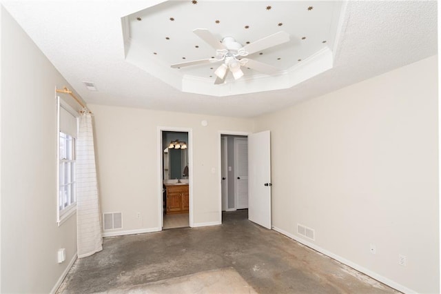 unfurnished bedroom with a tray ceiling, concrete floors, visible vents, and baseboards