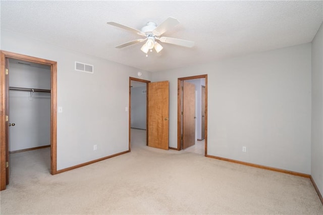 unfurnished bedroom featuring baseboards, a spacious closet, visible vents, and light colored carpet