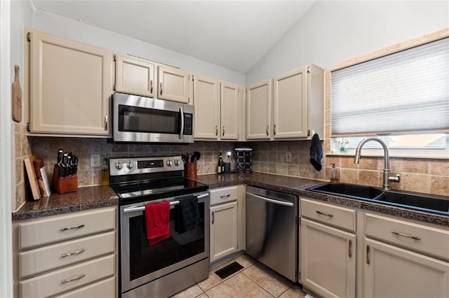 kitchen with a sink, tasteful backsplash, stainless steel appliances, light tile patterned floors, and vaulted ceiling