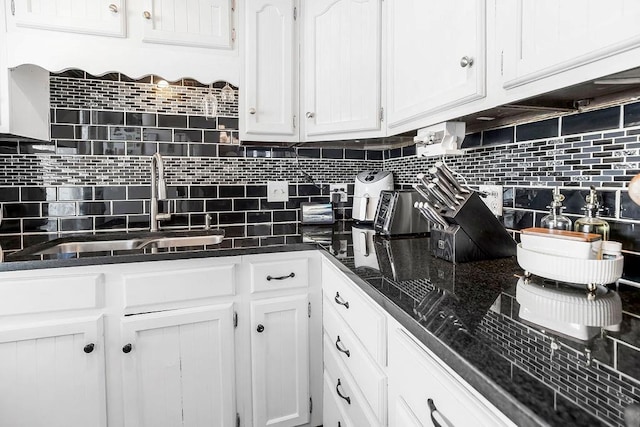 kitchen with dark stone counters, a sink, white cabinetry, and decorative backsplash