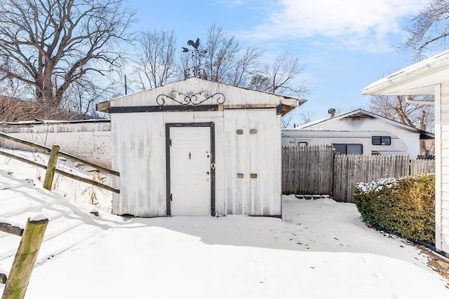 snow covered structure with an outbuilding, a storage unit, and fence