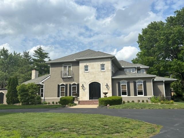 view of front of house featuring stone siding, a front lawn, a chimney, and stucco siding