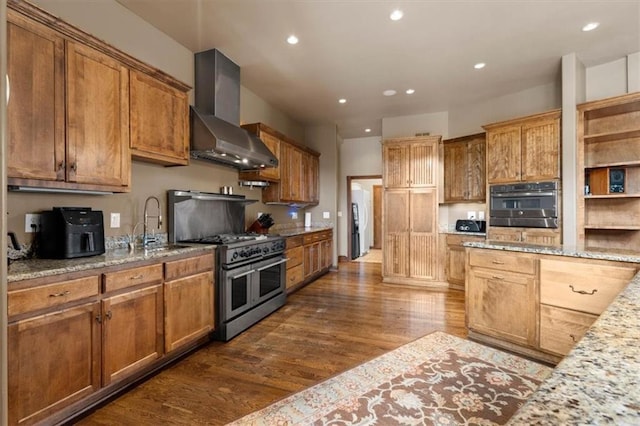 kitchen with light stone counters, stainless steel appliances, dark wood-style flooring, a sink, and wall chimney range hood