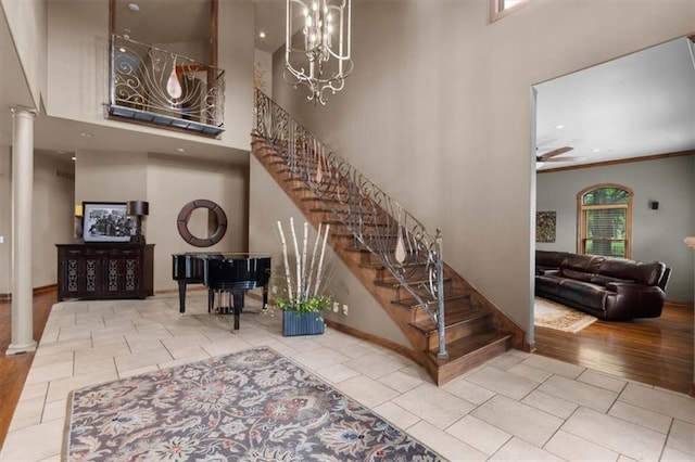 foyer with ceiling fan with notable chandelier, decorative columns, a towering ceiling, and stairs