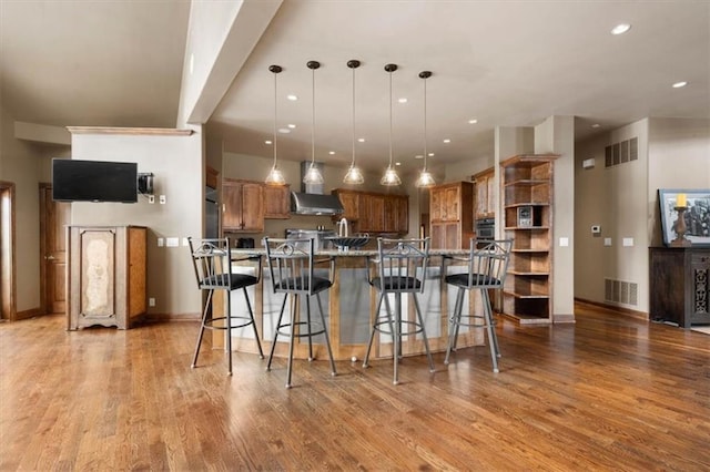 kitchen featuring hanging light fixtures, brown cabinetry, a kitchen bar, and visible vents