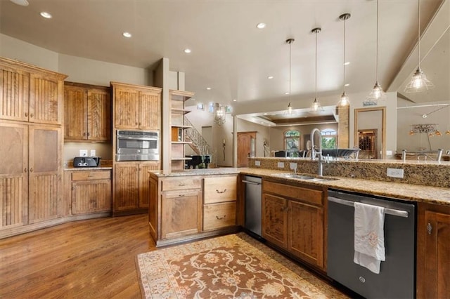 kitchen with stainless steel appliances, brown cabinetry, a sink, and pendant lighting