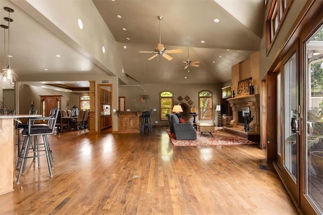 living area with a glass covered fireplace, wood finished floors, a high ceiling, and recessed lighting