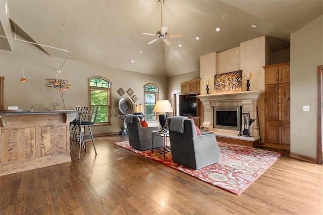 living room with high vaulted ceiling, a glass covered fireplace, light wood-style flooring, and a ceiling fan