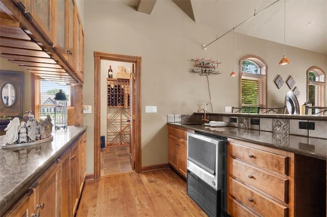 kitchen with a sink, hanging light fixtures, brown cabinets, dark stone counters, and light wood finished floors