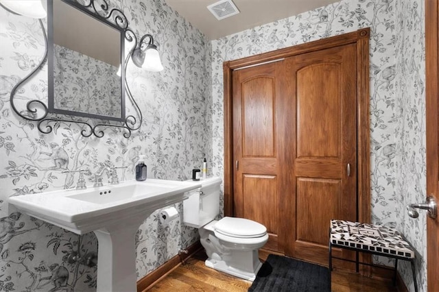 half bathroom with toilet, wood finished floors, visible vents, and wallpapered walls