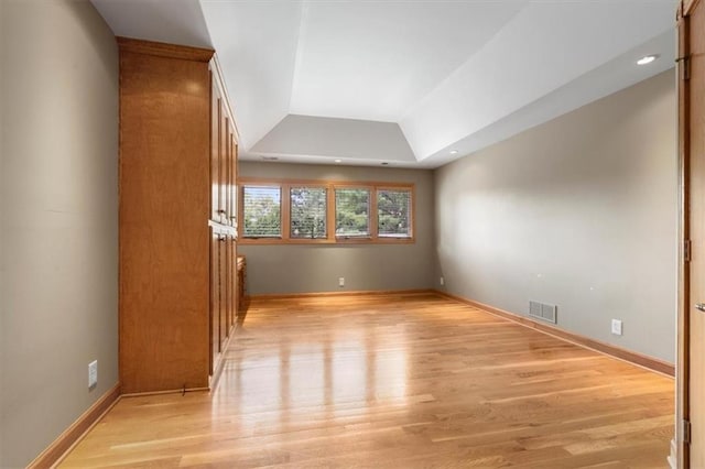 interior space featuring light wood-style floors, baseboards, visible vents, and a tray ceiling