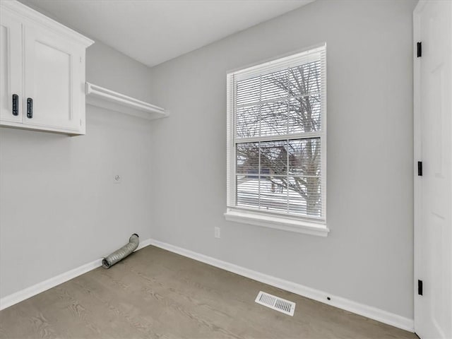 clothes washing area featuring cabinet space, baseboards, visible vents, and light wood-style flooring