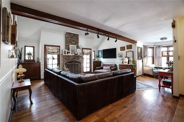 living room featuring dark wood-type flooring, vaulted ceiling with beams, a textured ceiling, a fireplace, and track lighting