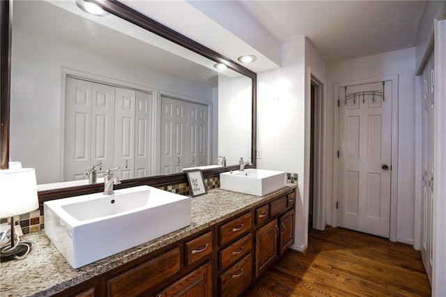 full bath with double vanity, wood finished floors, a closet, and a sink