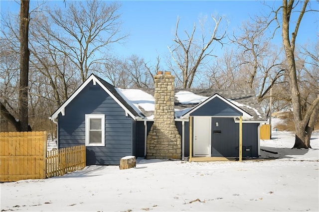 snow covered back of property featuring fence and a chimney