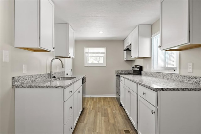 kitchen featuring white cabinets, light stone counters, stainless steel appliances, and a sink