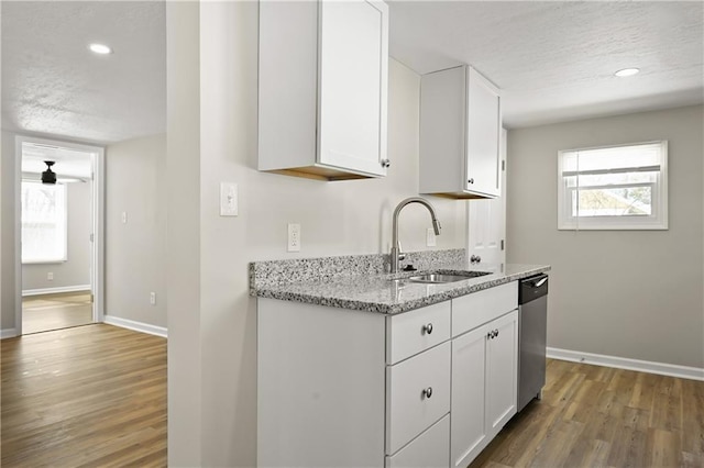 kitchen featuring light stone counters, white cabinets, a sink, a textured ceiling, and dishwasher