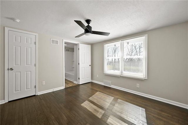 unfurnished bedroom with a textured ceiling, dark wood-type flooring, visible vents, and baseboards