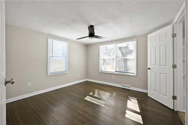 unfurnished bedroom with multiple windows, visible vents, and dark wood-style flooring