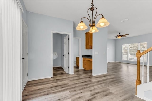 unfurnished living room featuring light wood-style floors, stairs, baseboards, and ceiling fan with notable chandelier