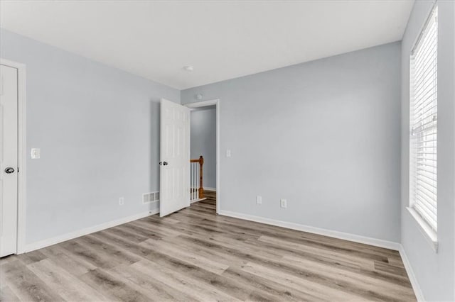 empty room with a healthy amount of sunlight, light wood-style floors, baseboards, and visible vents