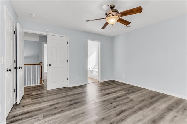 unfurnished bedroom with ensuite bath, baseboards, ceiling fan, and wood finished floors