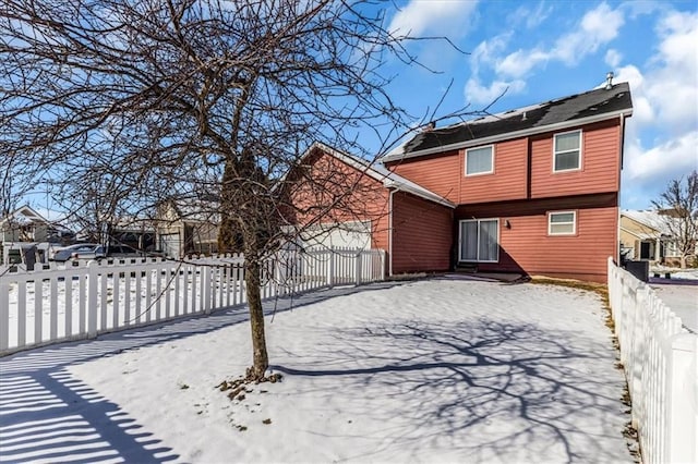 snow covered property with a garage and a fenced front yard