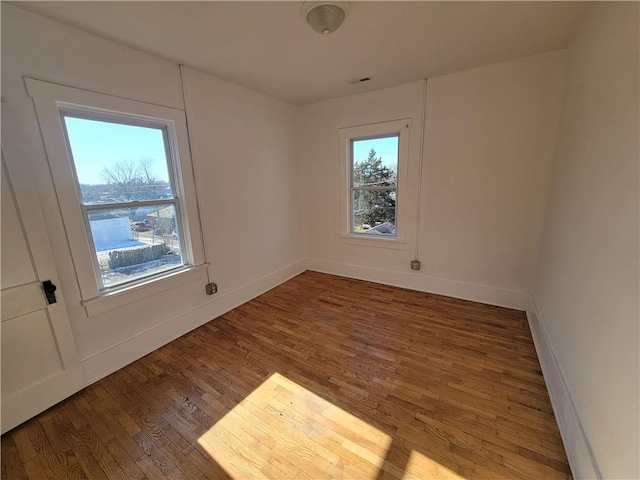 empty room with wood finished floors, visible vents, and baseboards