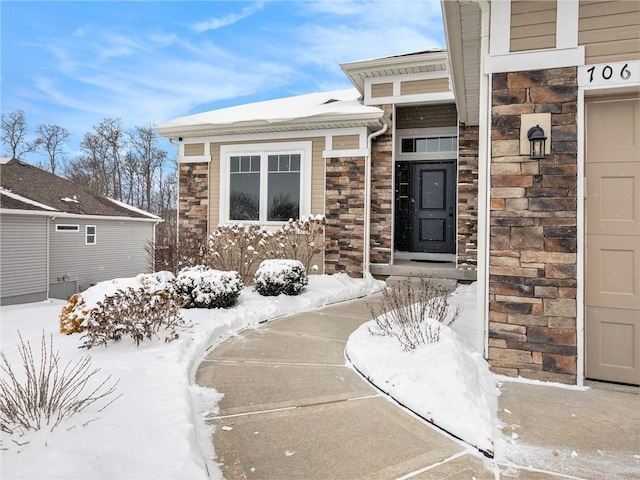 snow covered property entrance featuring stone siding