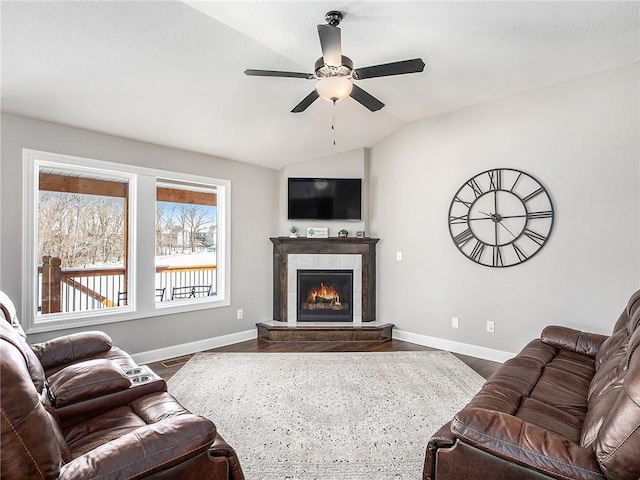 living area with a tile fireplace, a ceiling fan, baseboards, vaulted ceiling, and dark wood-style floors