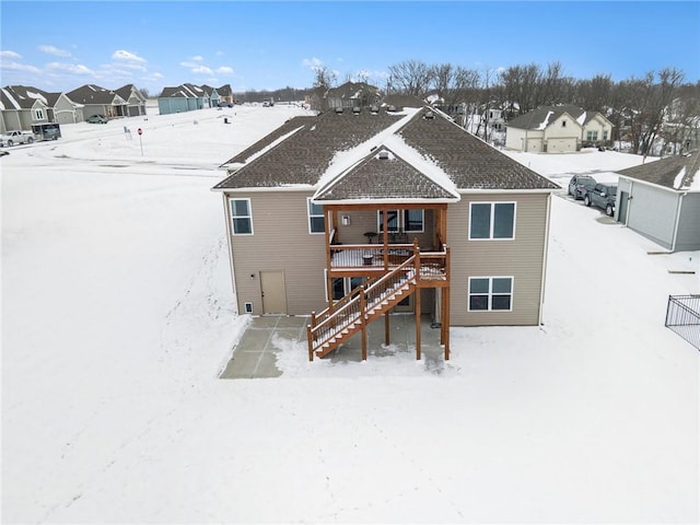 snow covered rear of property with stairs, a wooden deck, and a residential view